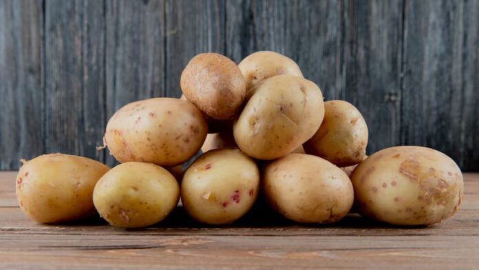Pile of yellow-brown potatoes stacked on a rustic wooden surface.