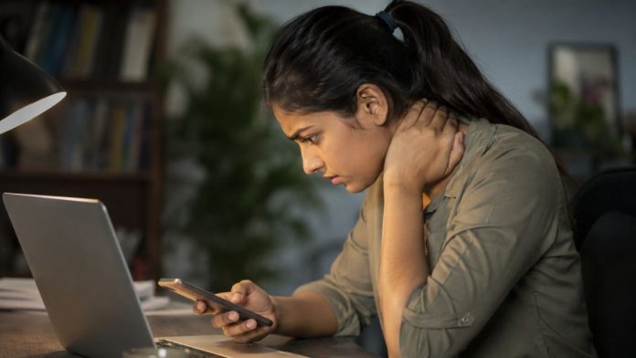 Woman using a laptop and smartphone while experiencing neck pain